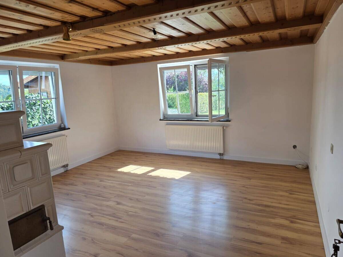 Heller Raum mit Holzdielenboden, sichtbaren Deckenbalken und einem traditionellen Kachelofen.