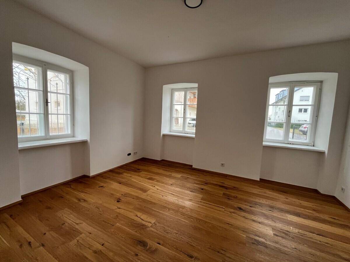 Heller, frisch renovierter Raum mit schönem Holzboden und mehreren Fenstern, die viel Tageslicht hereinlassen.