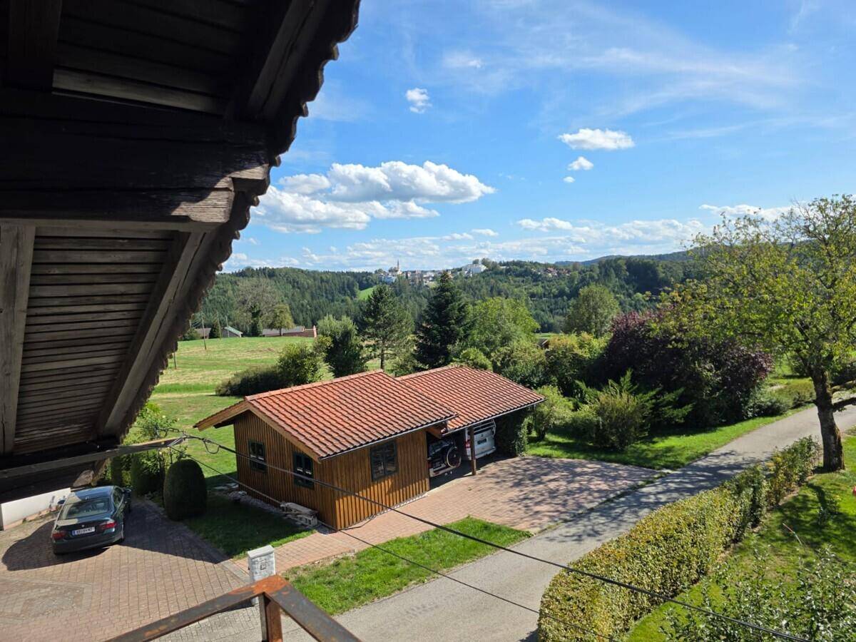 Weitblick über eine ländliche Landschaft mit einem kleinen Holzhaus, grünen Hügeln und einem Dorf in der Ferne.