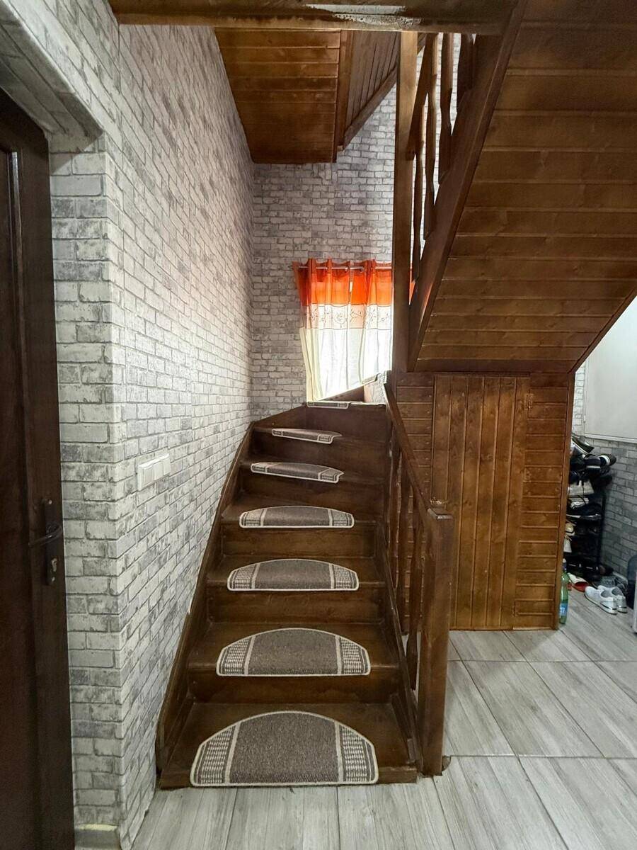 Holztreppe mit Teppichläufern und Ziegelsteinoptik-Tapete im Flurbereich des Hauses.