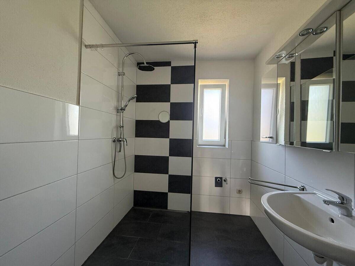 Modernes Badezimmer mit schwarz-weiß gefliester Dusche, Einzelwaschbecken und Spiegelschrank.