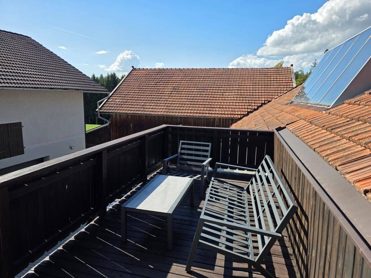 Gemütlicher Balkon mit Holzfußboden und Gartenmöbeln, mit Blick auf Ziegeldächer und Solaranlagen.
