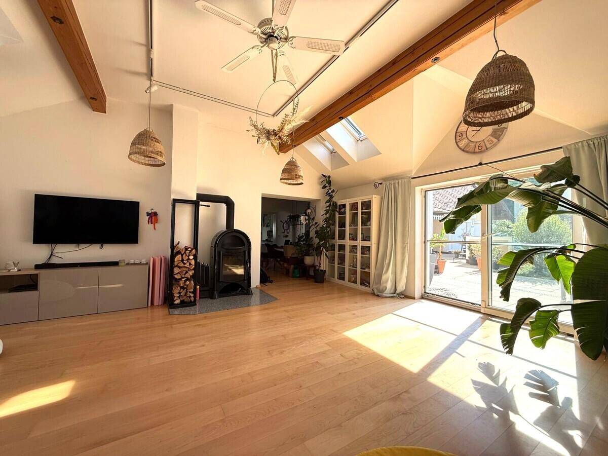 Gemütliches Wohnzimmer mit Kaminofen, Holzboden, hohen Decken und direktem Zugang zur Terrasse.