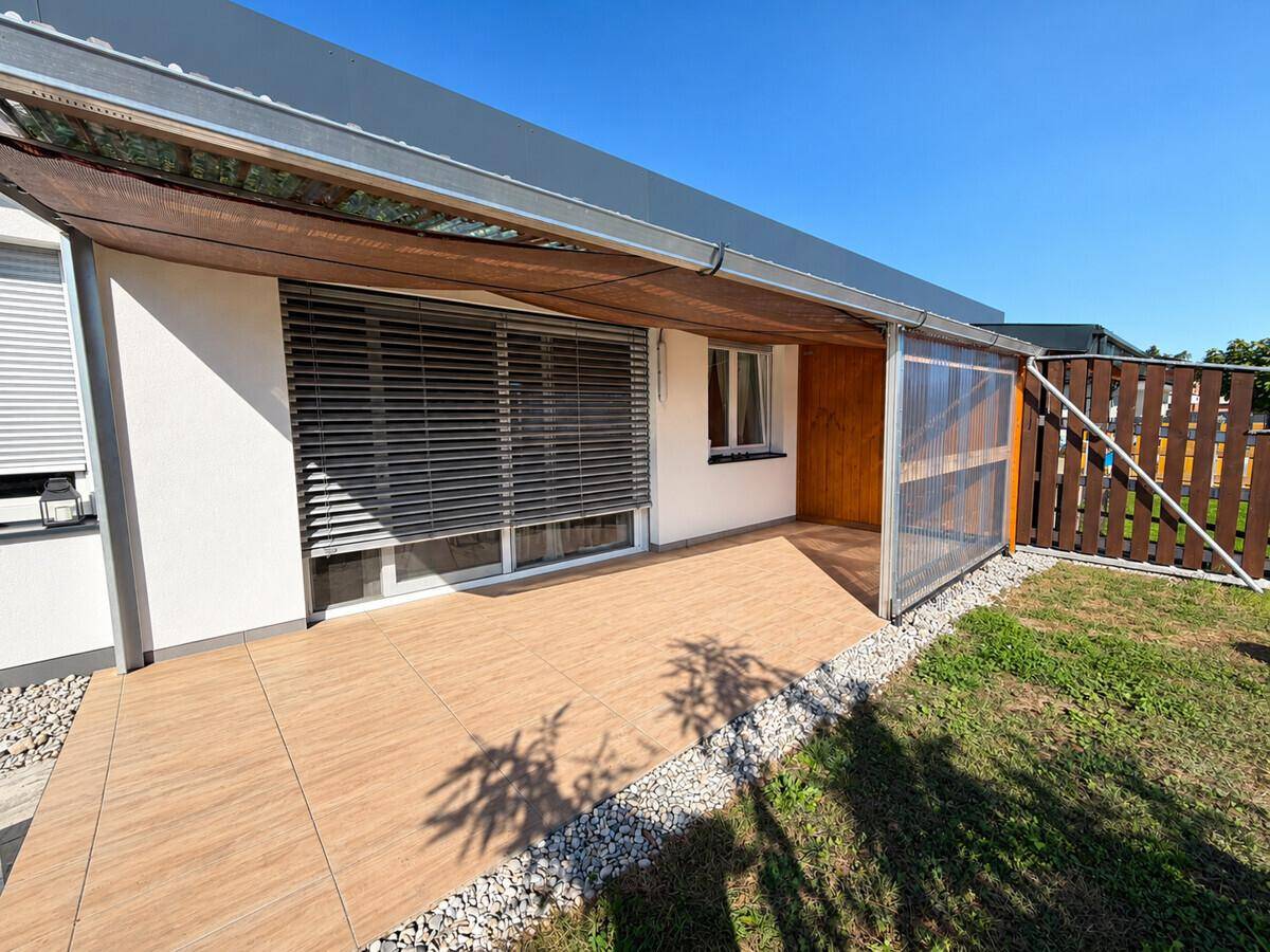 Überdachte Terrasse mit Fliesenboden und Blick auf den Gartenbereich.