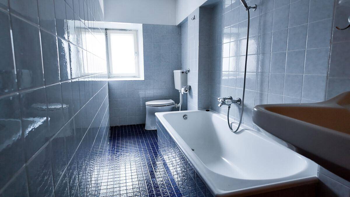 Badezimmer mit blauen Fliesen, Badewanne, Toilette und einem Fenster für Tageslicht.