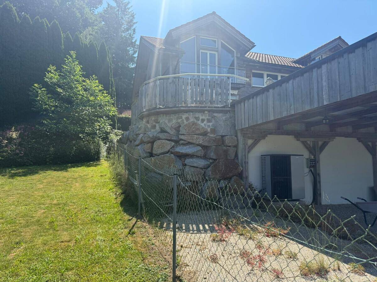 Rustikales Haus mit Steinfundament, Balkon und überdachtem Stellplatz im Grünen.