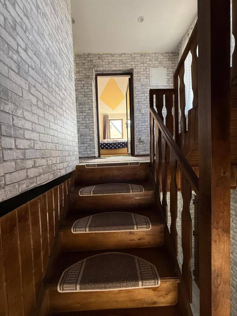 Holztreppe mit Teppichläufern und Ziegelsteinoptik-Tapete, führt zu einem Schlafzimmer.