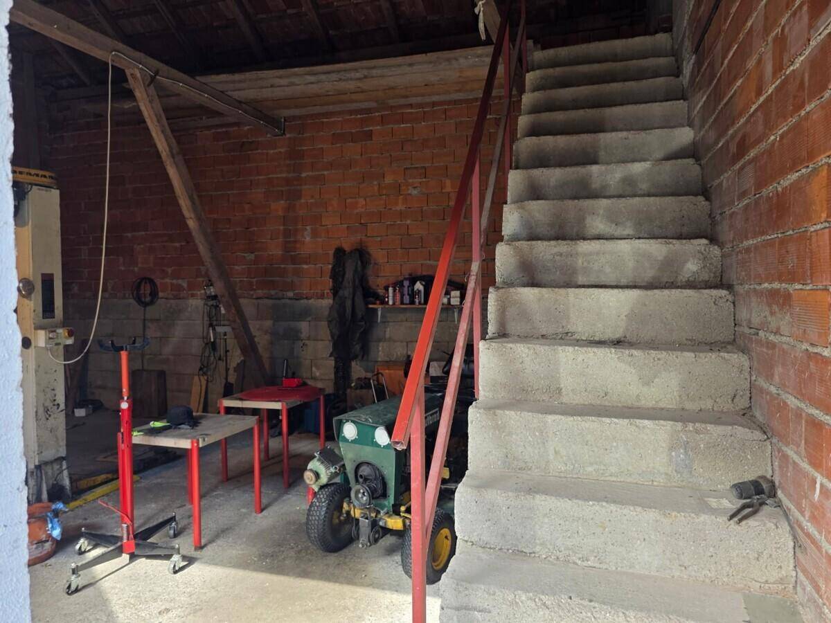 Innenansicht einer Garage oder Werkstatt mit Betontreppe, Ziegelwänden und verschiedenen Geräten.
