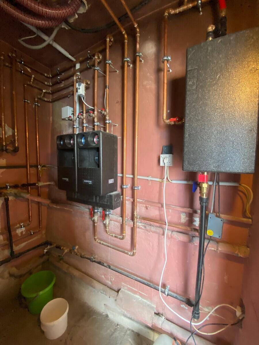 Technikraum mit komplexen Rohrleitungen und Heizungsinstallationen an der Wand.