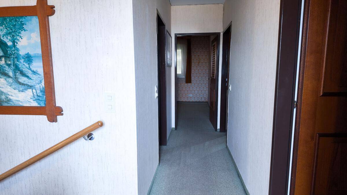Langer, schmaler Flur mit mehreren Türen und einem Handlauf an der Wand.