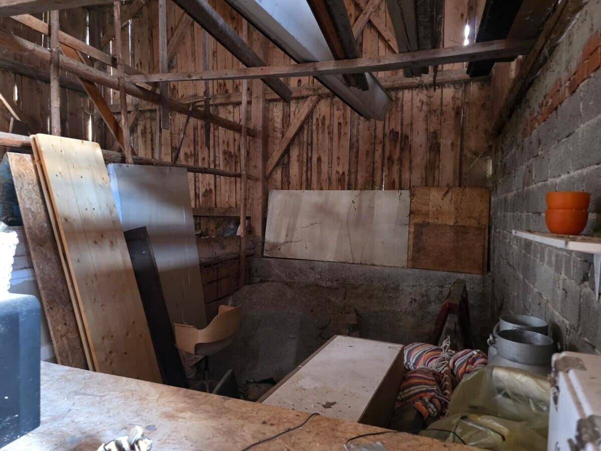 Innenansicht einer rustikalen Holzscheune mit gemauerten Wänden und gelagerten Gegenständen.