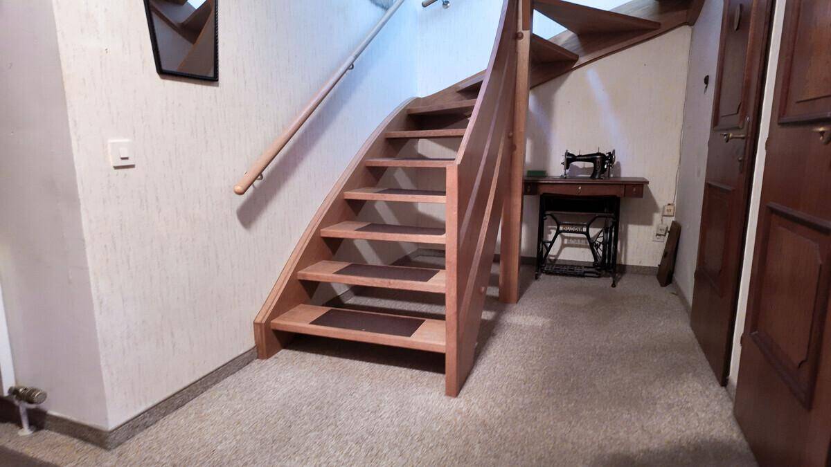 Holztreppe mit Teppichstufen in einem Flurbereich, daneben eine alte Nähmaschine als Dekoration.