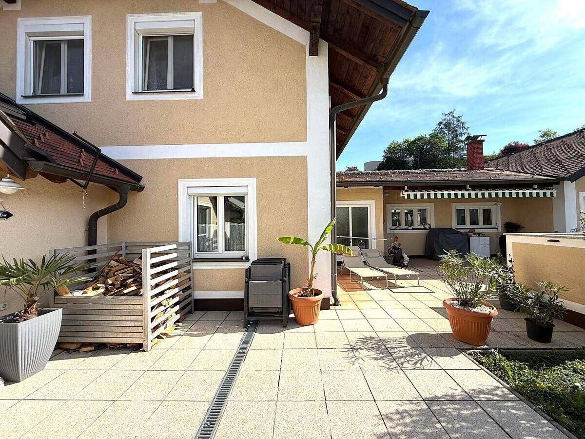 Geräumige Terrasse mit Liegestühlen, Holzstapel und einem angenehmen Blick auf den Garten.
