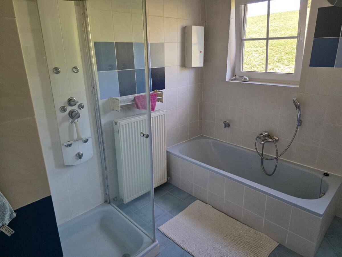 Badezimmer mit Badewanne, Duschkabine, blauen und weißen Fliesen sowie einem Fenster.