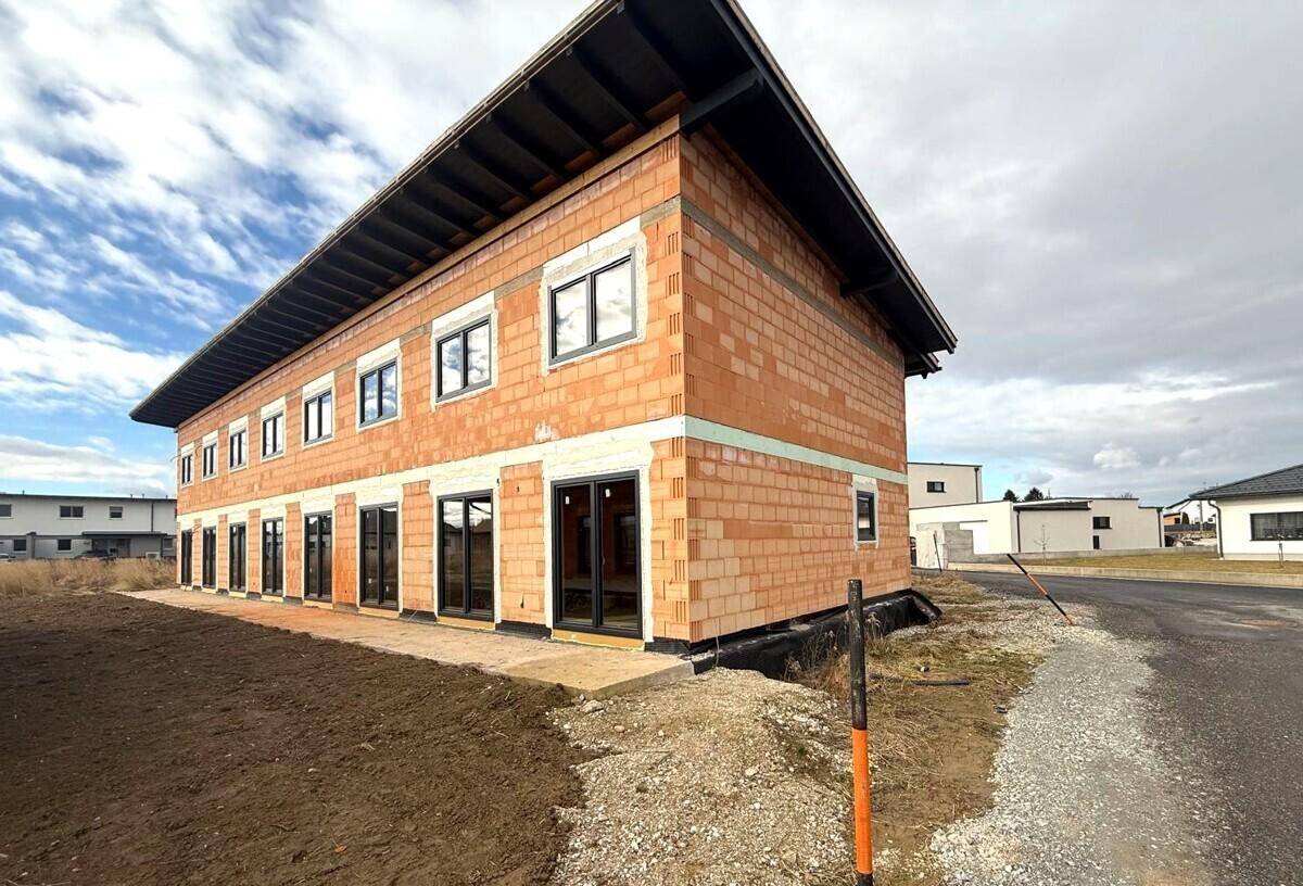 Seitenansicht eines im Bau befindlichen Gebäudes mit Ziegelmauerwerk und modernen Fensterrahmen.