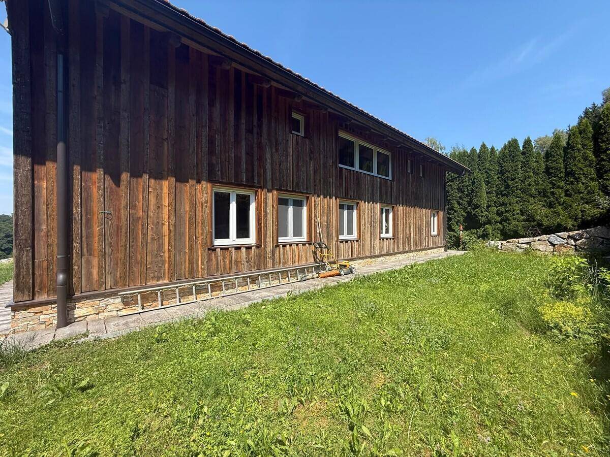 Seitenansicht eines Holzhauses mit weißen Fenstern und einer grünen Rasenfläche.