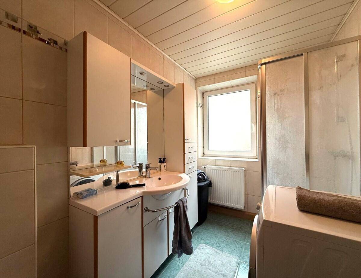 Badezimmer mit Duschkabine, Einzelwaschbecken und Fenster für Tageslicht.