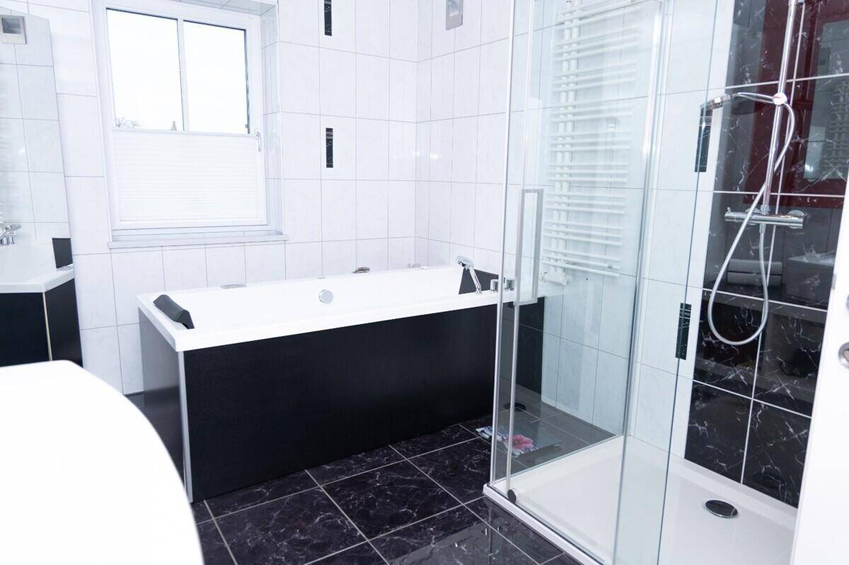 Modernes Badezimmer mit Badewanne, Duschkabine, weißen Wandfliesen und dunklem Boden.