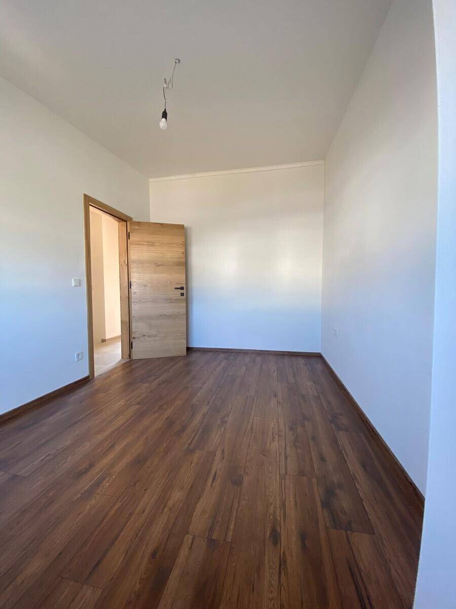 Helles, unmöbliertes Zimmer mit ansprechendem Holzboden und einer modernen Holztür.