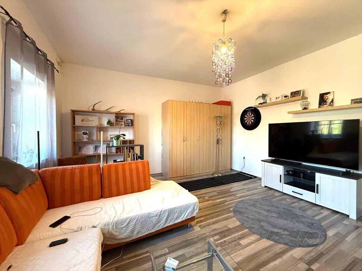 Gemütliches Wohnzimmer mit orangefarbenem Sofa, Fernseher und Regalen, hell beleuchtet.