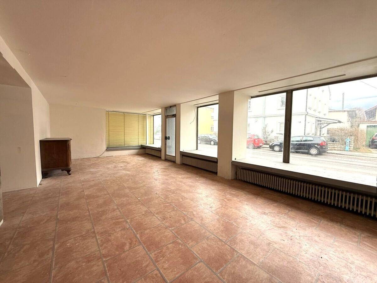 Großer, heller Raum mit Fliesenboden und großen Fenstern zur Straße.