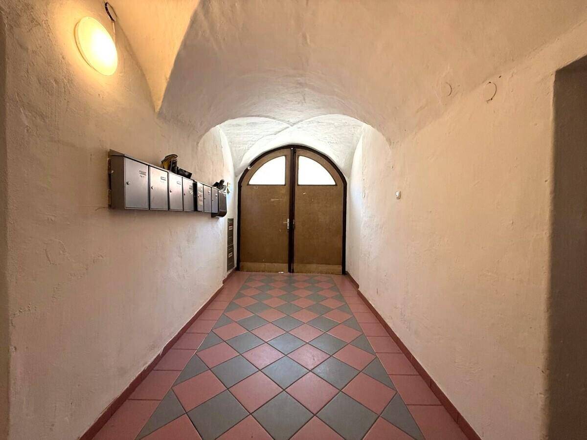 Historischer Flur mit Gewölbedecke, gemustertem Fliesenboden und einer großen Holztür am Ende.