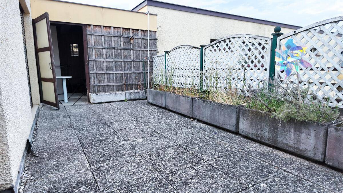 Gepflasterte Terrasse mit Betonkübeln und einem Holzzaun, ideal für entspannte Stunden im Freien.
