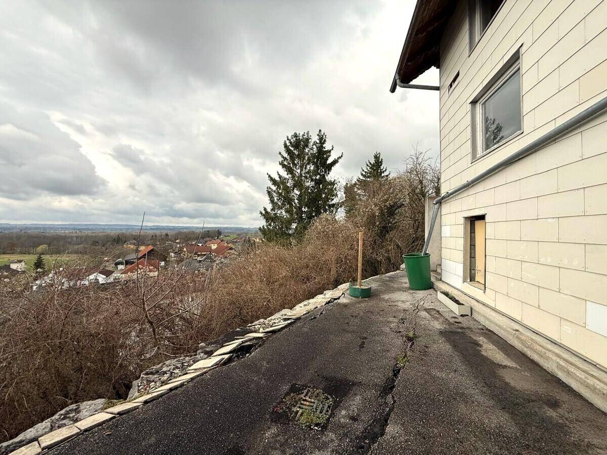 Seitenansicht eines Gebäudes mit heller Fassade und weitem Blick über die Landschaft und Siedlung.