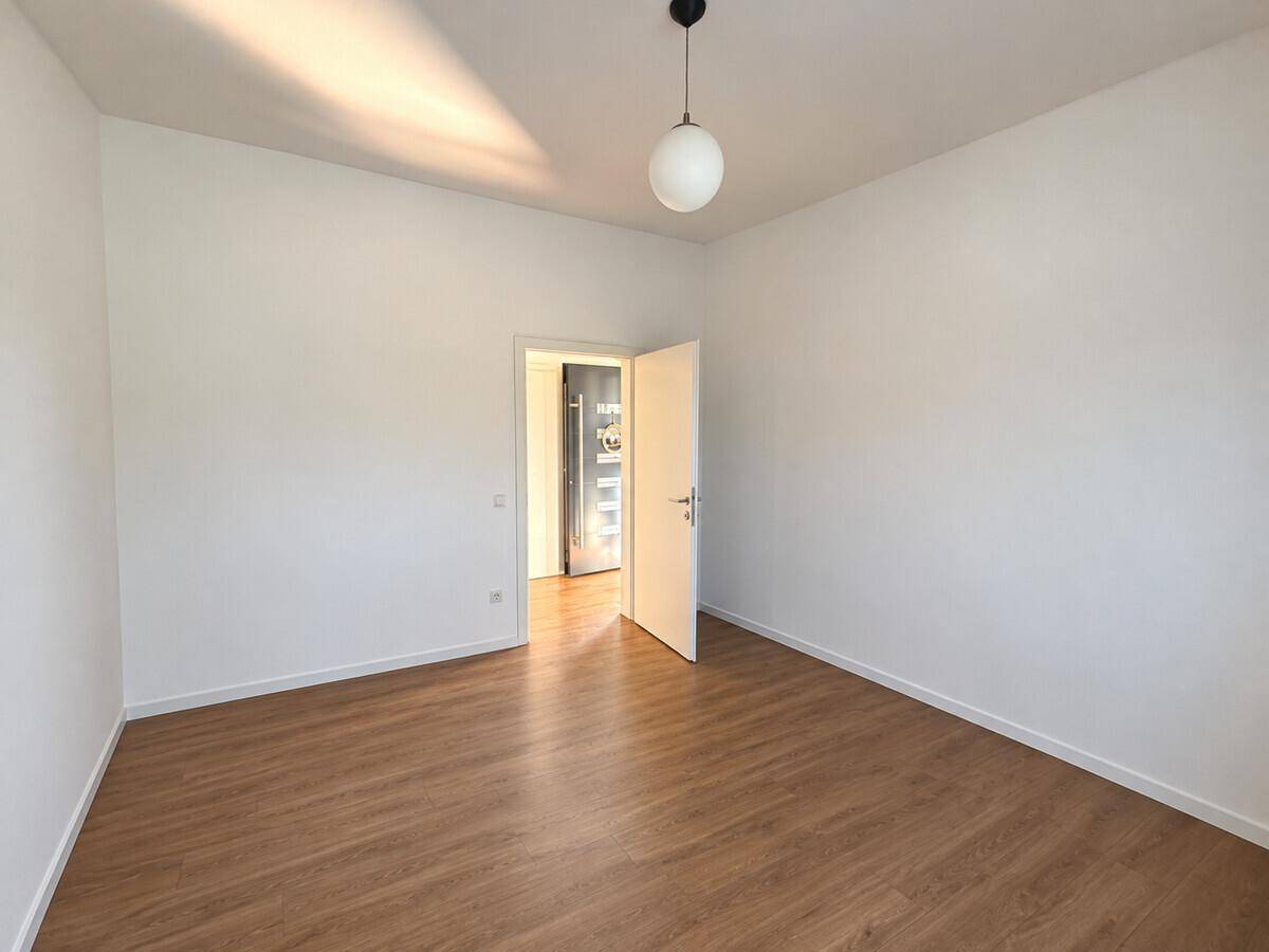 Leerer Raum mit hellem Laminatboden und weiß gestrichenen Wänden.