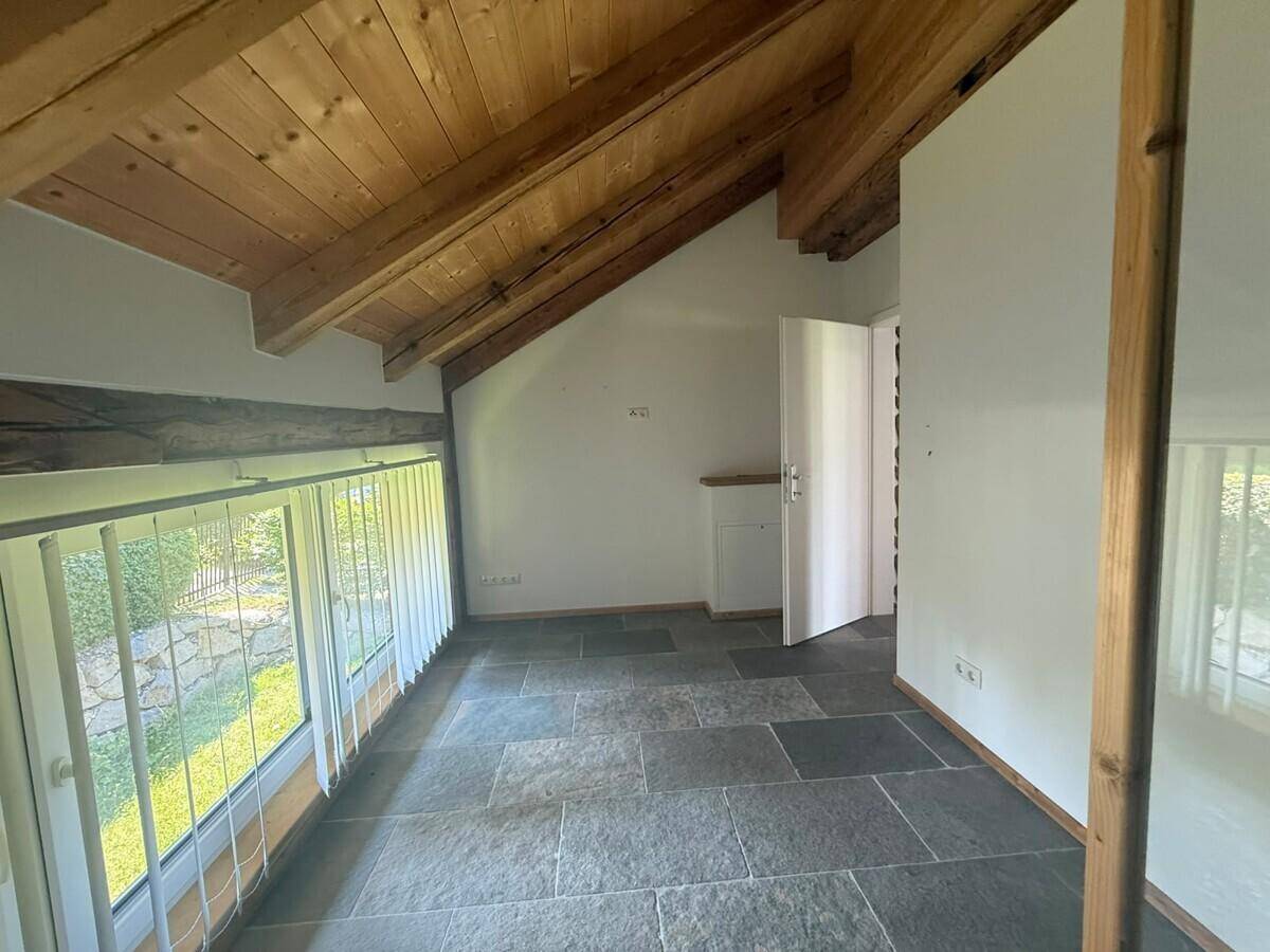 Heller Raum im Dachgeschoss mit Holzbalkendecke, Schieferboden und Blick ins Grüne.