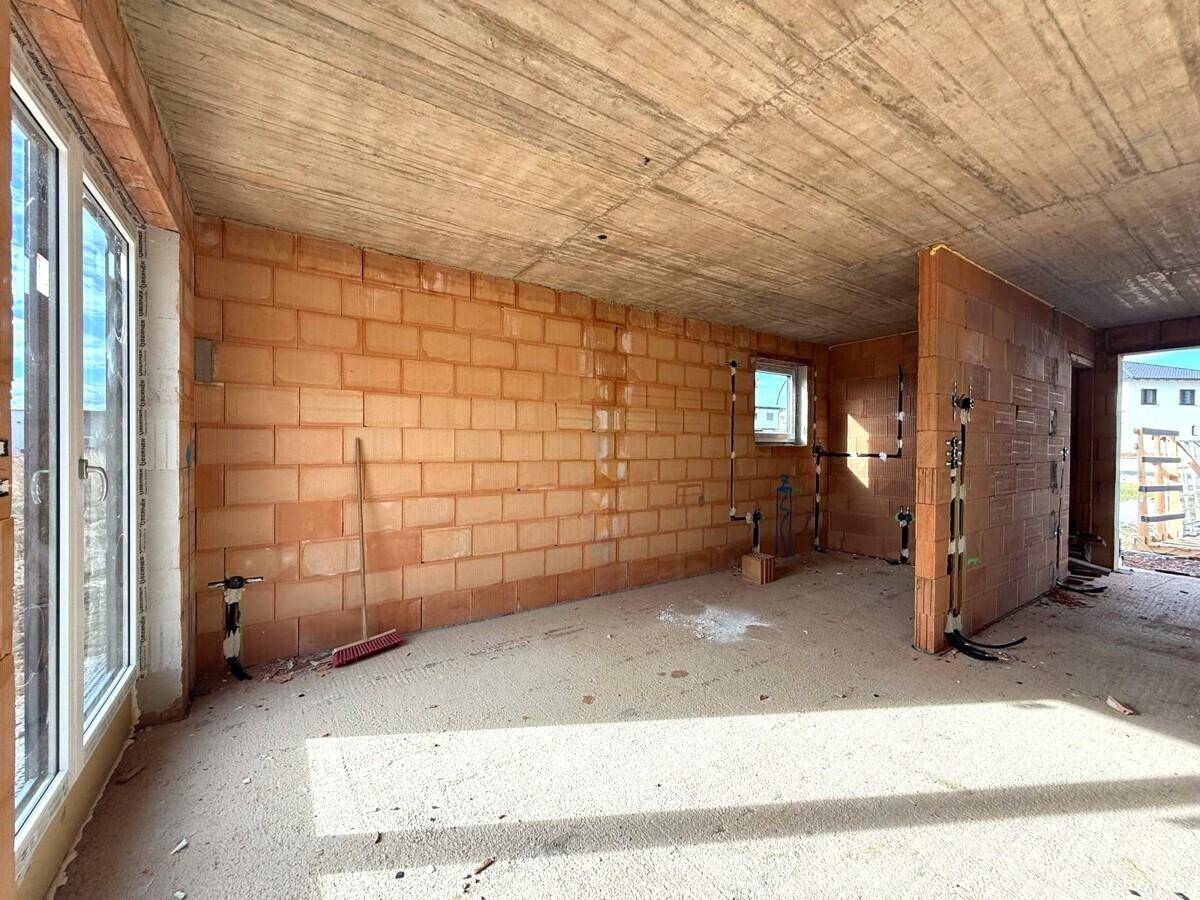 Innenansicht eines Rohbaus mit unverputzten Ziegelwänden, Beton-Decke und großen Fensteröffnungen.