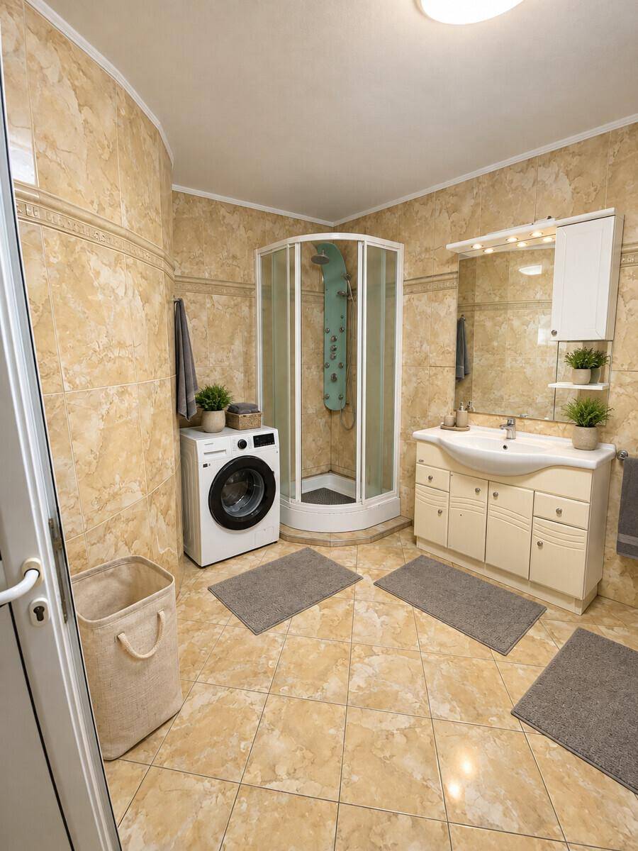 Gefliestes Badezimmer mit Duschkabine, Waschbeckenunterschrank und Waschmaschine.