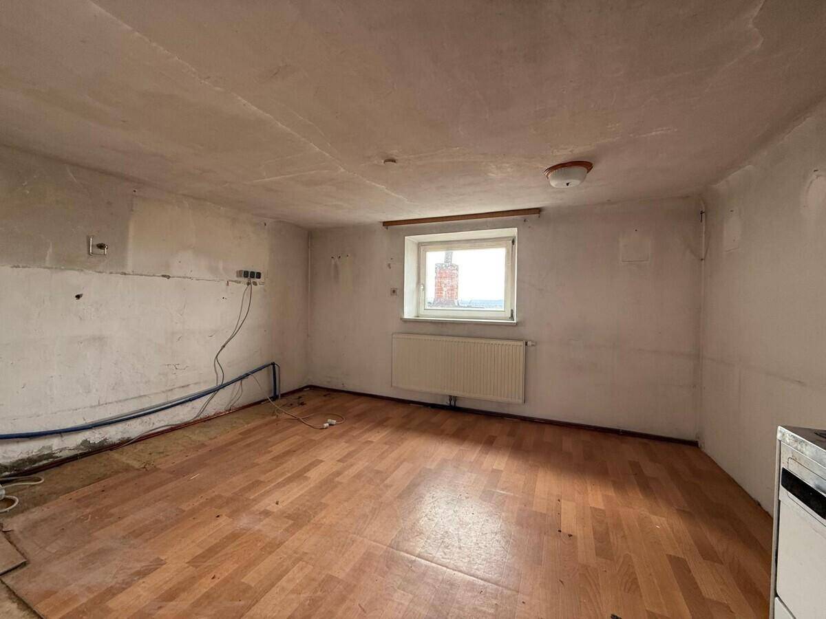 Leerer Raum mit Holzdielenboden, einem Fenster und sichtbaren Installationen an den Wänden, bereit für Renovierung.