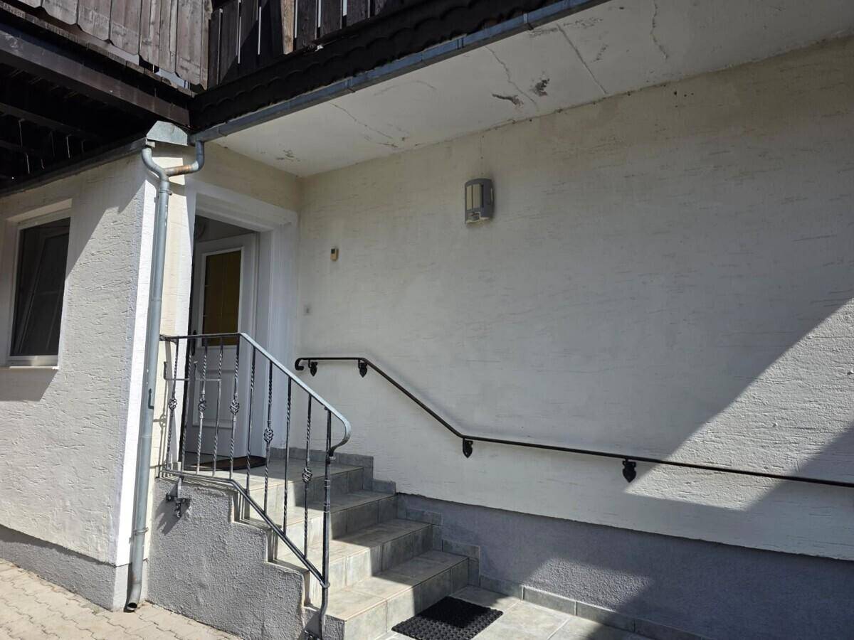 Eingangsbereich des Hauses mit Steintreppe, schmiedeeisernem Geländer und heller Putzfassade.