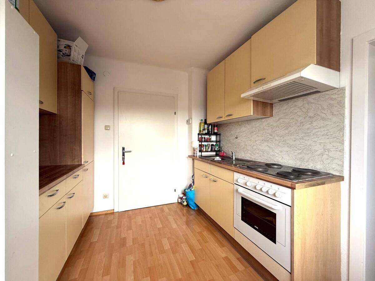 Funktionale Küche mit hellen Holzschränken, Laminatboden und integriertem Backofen.