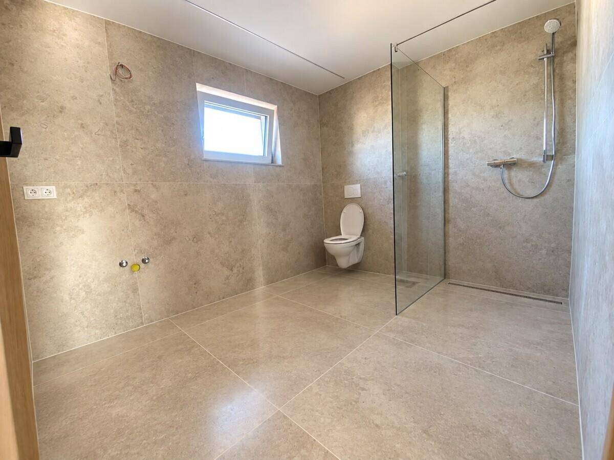 Geräumiges Badezimmer mit begehbarer Dusche, wandhängender Toilette und hellen Fliesen, mit Fenster.