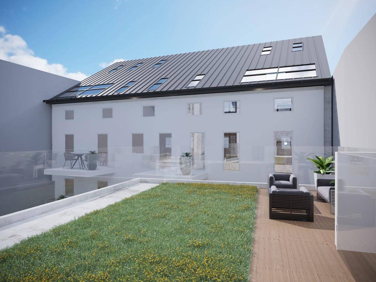 Rückansicht des Gebäudes mit modernem Satteldach, Dachfenstern und einer großzügigen Dachterrasse mit Rasenfläche und Sitzgelegenheiten.