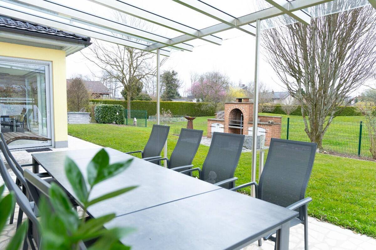 Überdachte Terrasse mit großem Esstisch und Grillplatz im weitläufigen Gartenbereich.