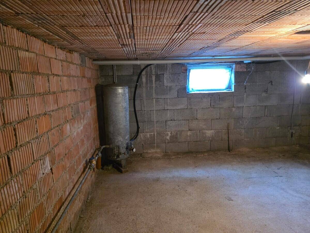 Unfertiger Kellerraum mit Ziegel- und Betonwänden, kleinem Fenster und Warmwasserbereiter.