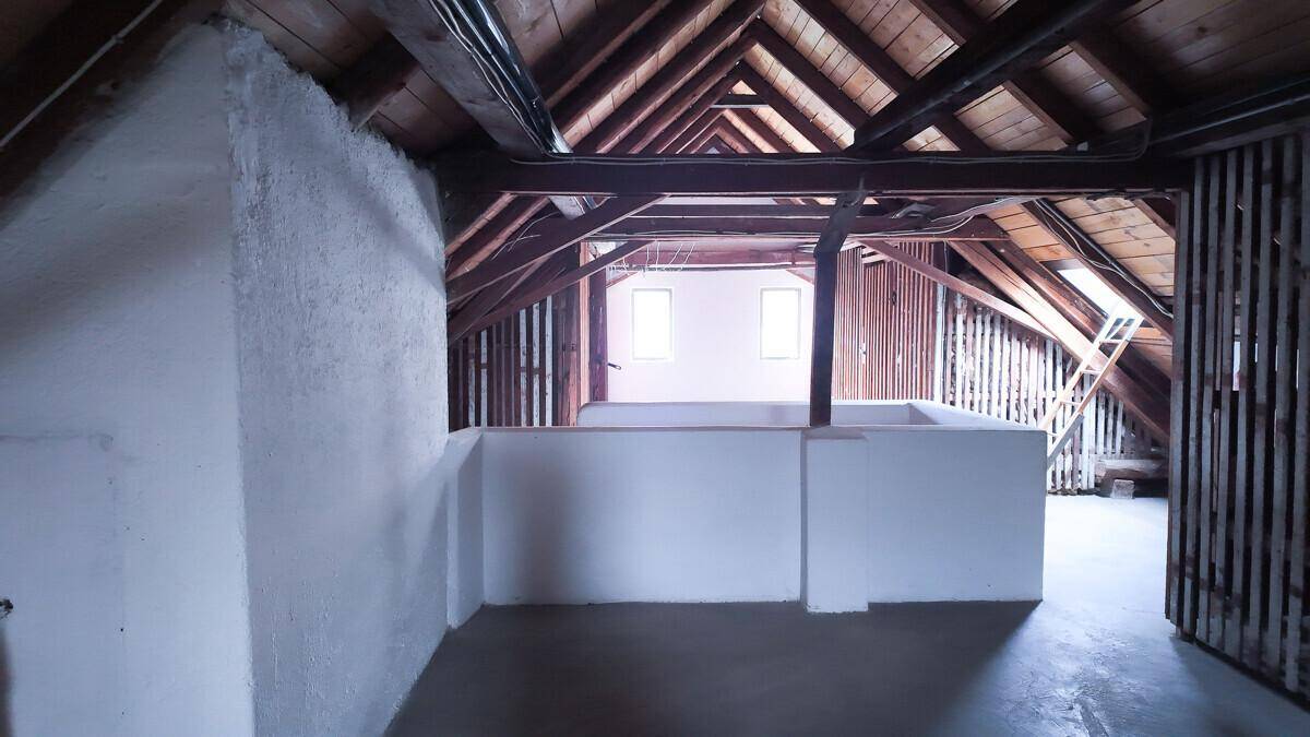 Geräumiger Dachboden mit sichtbaren Holzbalken und zwei kleinen Fenstern, bereit zum Ausbau.
