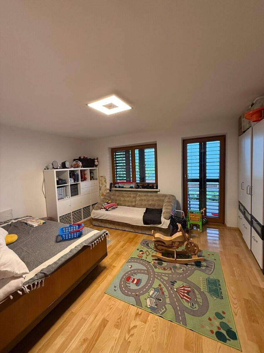Kinderzimmer mit Holzboden, Spielteppich und Fenster mit Jalousien.