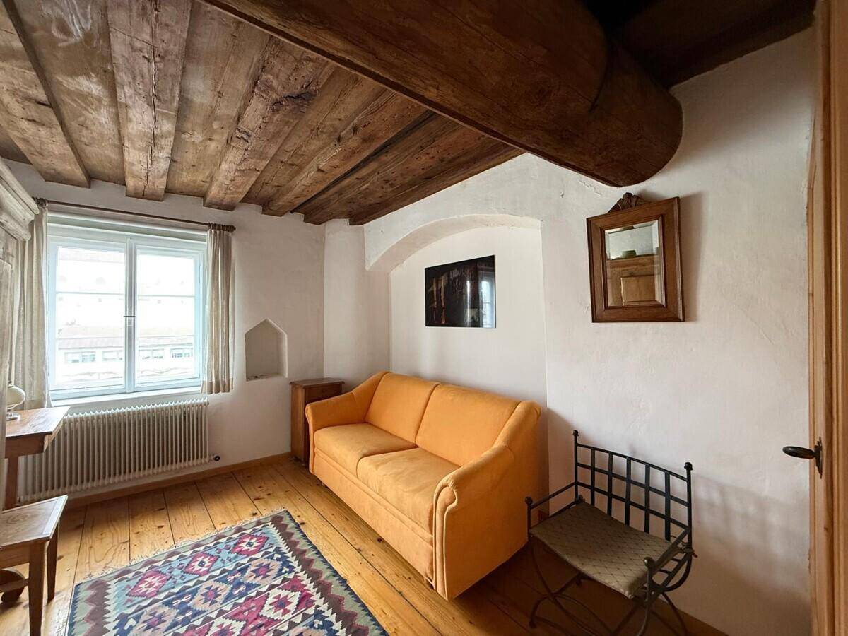 Gemütliches Zimmer mit orangefarbenem Sofa, Holzbalken und breiten Dielenböden.