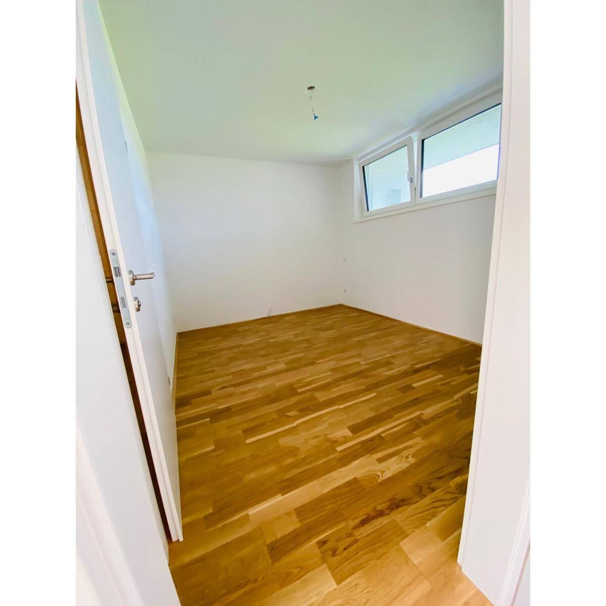Kleines, helles Zimmer mit Holzboden und einem Fenster, ideal als Schlaf- oder Arbeitszimmer.