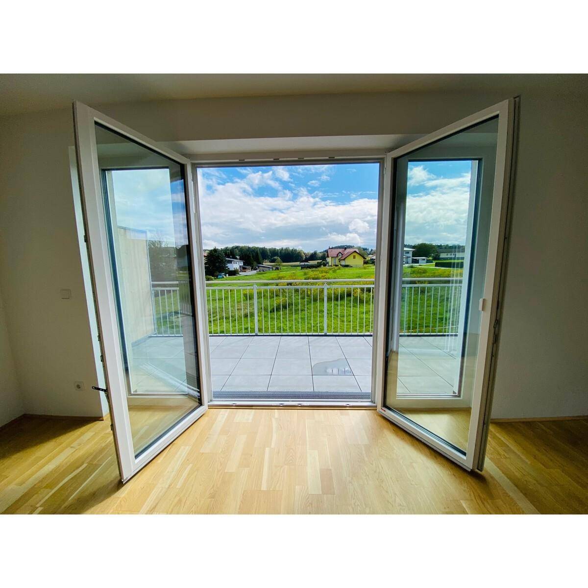 Geräumiges Zimmer mit Holzboden und großen Fenstertüren, die einen weiten Blick ins Grüne bieten.