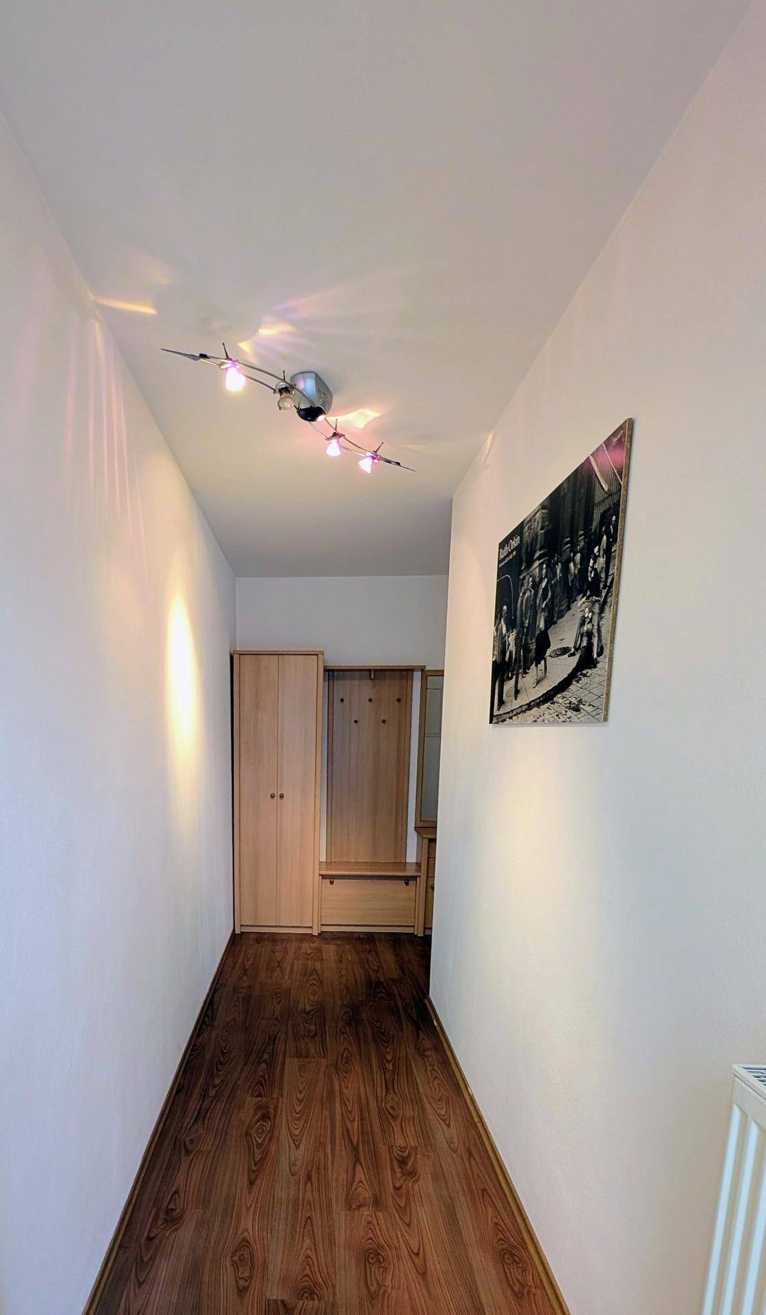 Heller Flur mit Laminatboden, weißen Wänden und praktischen Garderobenmöbeln aus Holz.