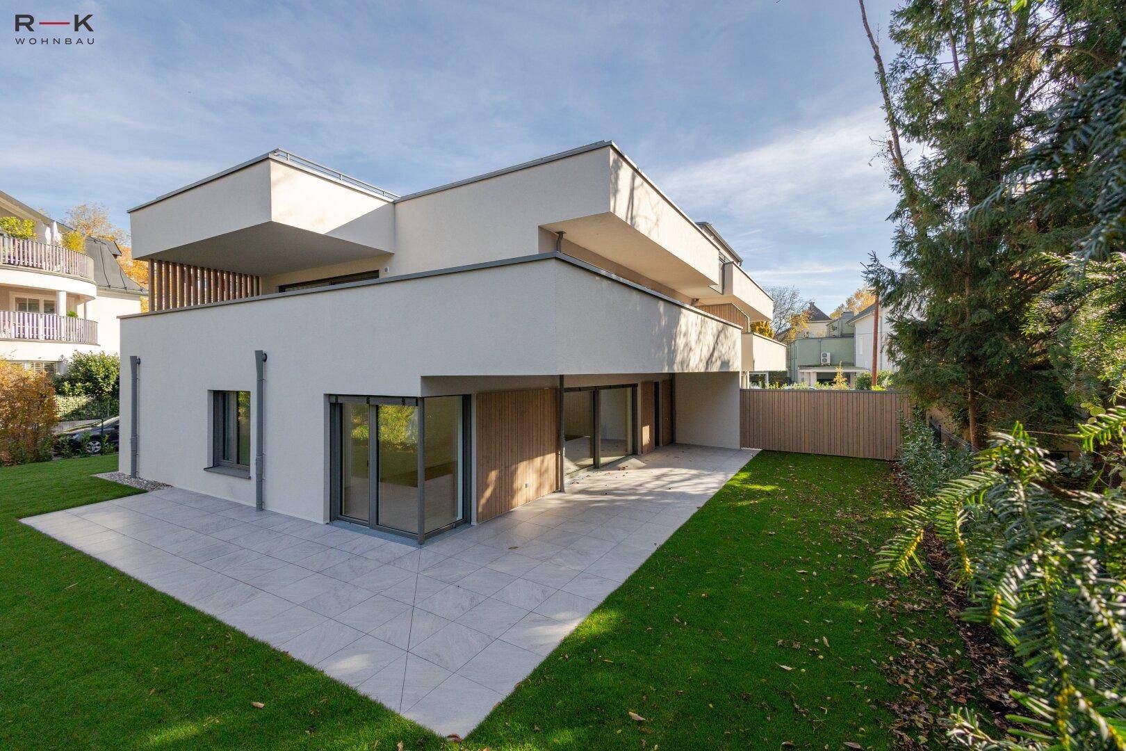 Moderne Wohnanlage mit gepflegtem Rasen und großer Terrasse, umgeben von Bäumen.