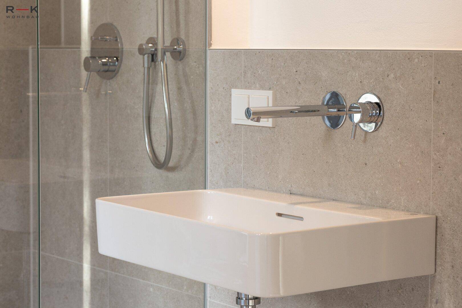 Modernes Waschbecken mit Wandarmatur und grauen Fliesen in einem stilvollen Badezimmer.