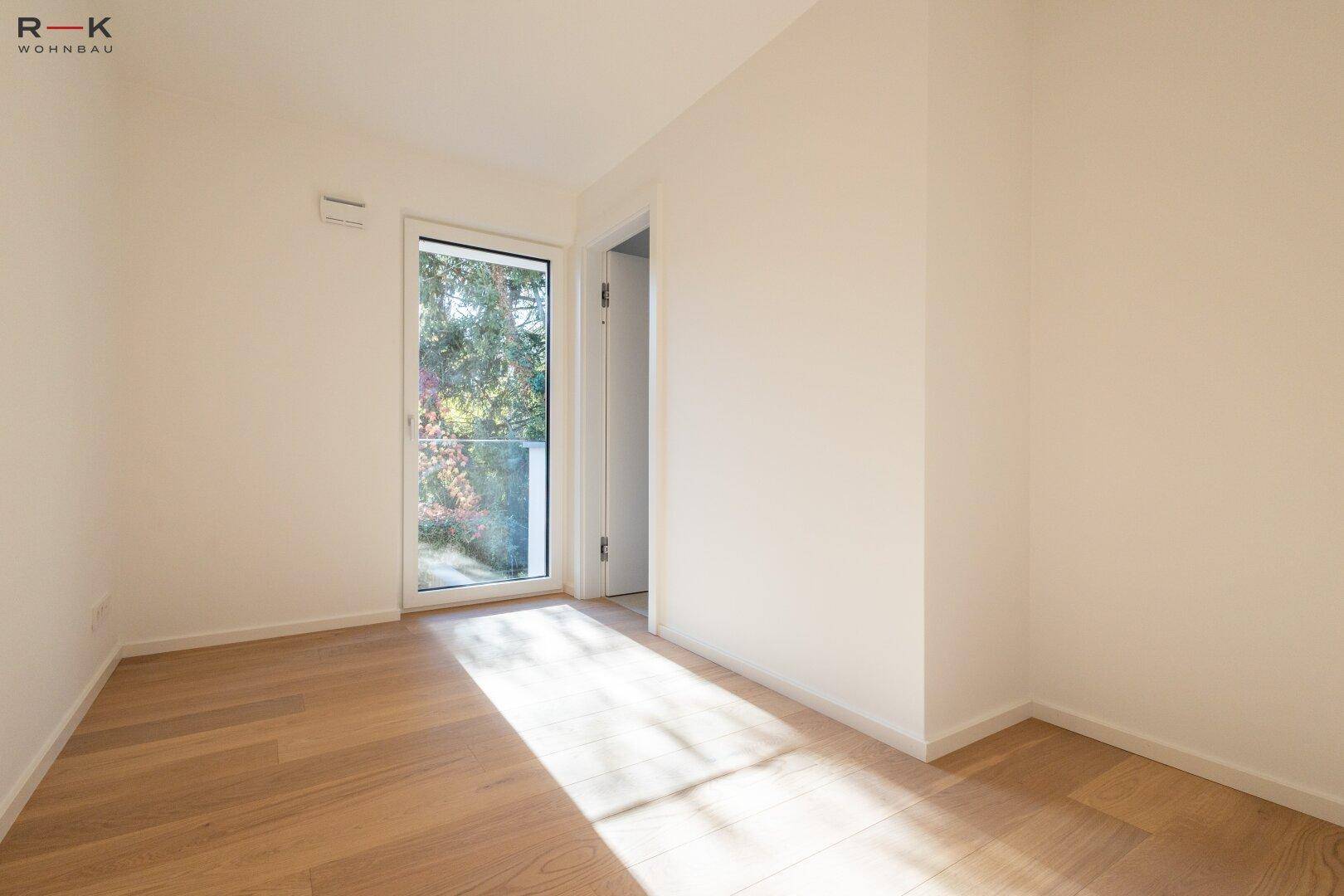 Helles Zimmer mit Parkettboden und Zugang zu einem kleinen Balkon, ideal als Kinder- oder Gästezimmer.