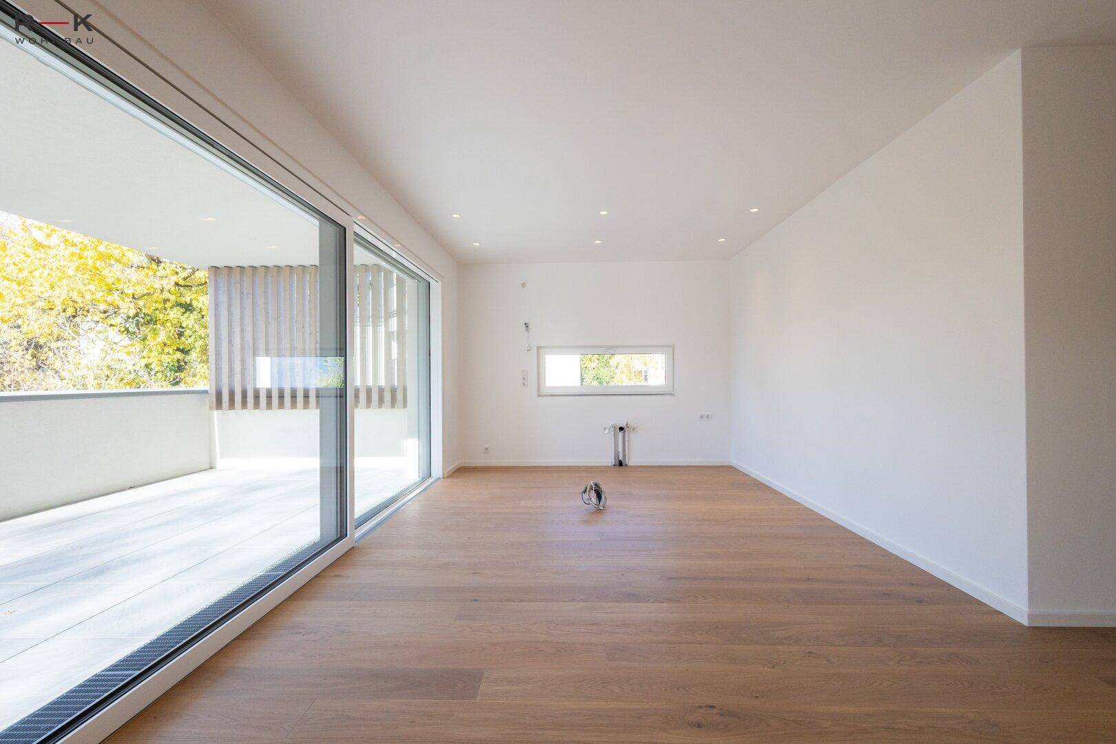 Geräumiges Wohnzimmer mit großen Schiebetüren, die viel Tageslicht hereinlassen und zum Balkon führen.