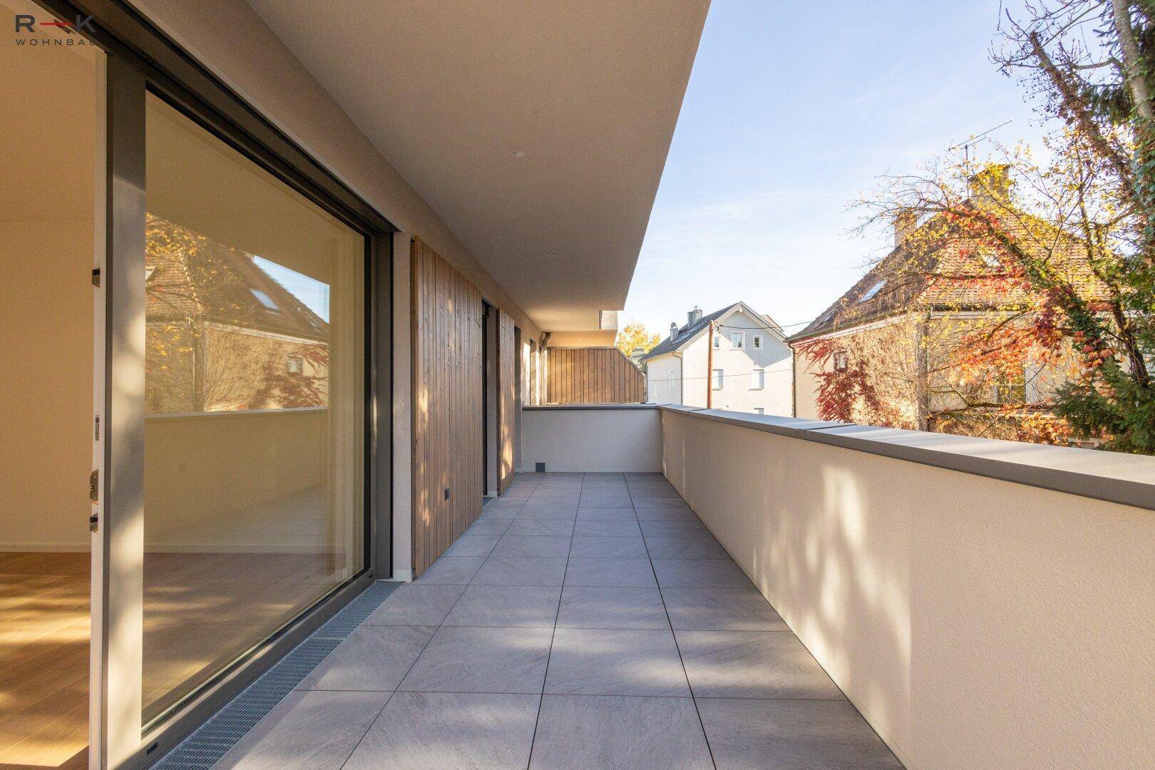 Langer, gefliester Balkon mit Blick auf die umliegenden Häuser und Bäume.